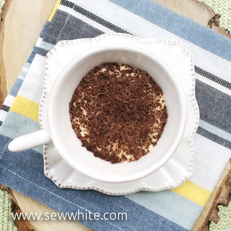 white cup and saucer with Tiramisu with Tea with chocolate shavings on top