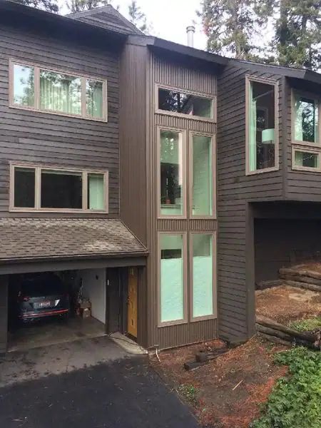 Exterior view of a dark brown modern home in Coeur D'Alene, Idaho, featuring large windows, vertical siding, and an attached garage with a car.