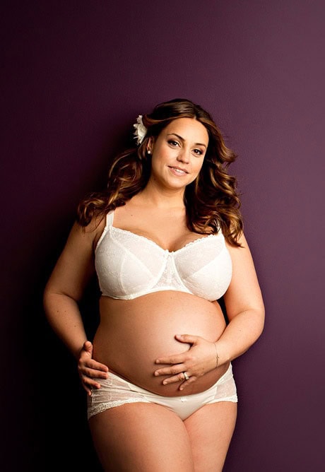 Elegante gravidfotografering av kvinne med mage, i hvit undertøy, mot mørk lilla bakgrunn. Perfekt for magefotografering og feiring av graviditet.