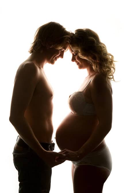 Par glad gravid kvinne og mann som holder hender foran mage, silhuett, kjærlighet, gravidfotografering, gravidfoto, unikt øyeblikk, intime bilder, familieforberedelse, vakkert minne, graviditetssyklus.