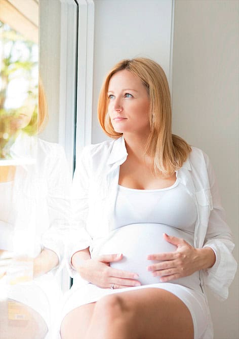 Glad gravid kvinne som nyter øyeblikket foran et vindu, symbol på ro og forventning under graviditeten. Naturlig lys fremhever den skjønnheten og styrken i en gravid kvinne. Perfekt for gravidfotografering.