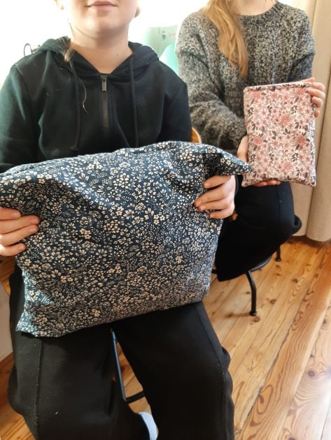 Deux adolescents montrent fièrement leurs créations textiles : un coussin et une pochette pour livres.