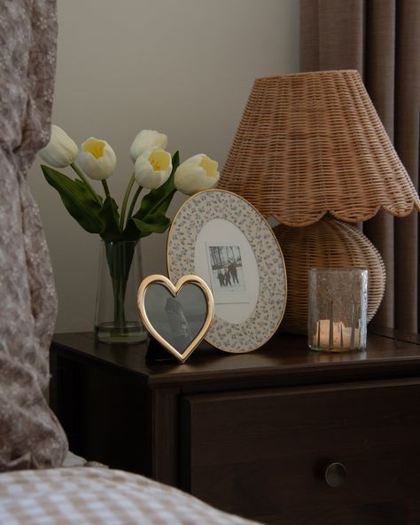 Dark wood nightstand styled with a vase of fresh flowers, a lamp, and small photo frames — elegant and timeless bedside table decor ideas from By Paige Nicole.