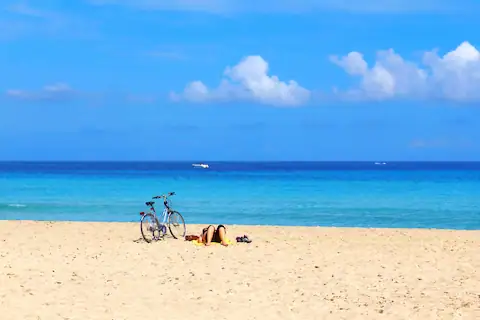 Hombre en la playa recostado y junto a el su bicicleta