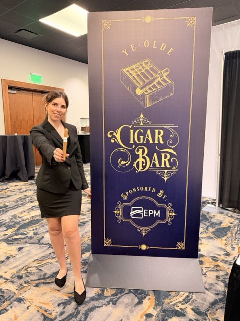 Cigar Bella Cigar Roller at a Sponsored Event Cigar Bella cigar roller holding a finished cigar beside a Cigar Bar sponsor display