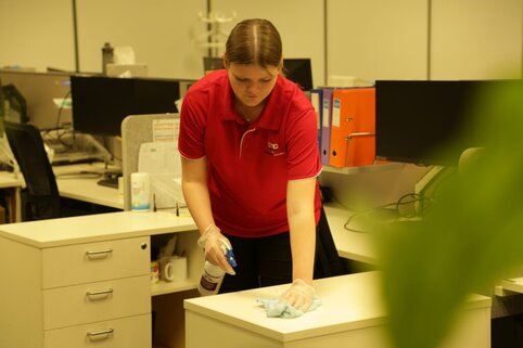 AMC Commercial Cleaning female young cleaner in uniform cleaning workstation, sanitising surfaces in Sydney office