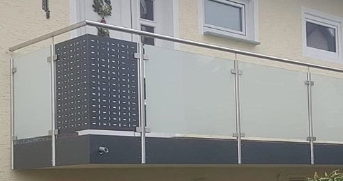 Modernes Balkongeländer von Stahl- und Metallbau Drost mit Edelstahlhandlauf, satinierten Glaspaneelen und einer perforierten dunkelgrauen Sichtschutzwand.