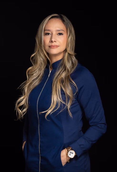 Foto de perfil profissional de médica de jaleco azul-marinho em fundo preto, feita no estúdio em BH