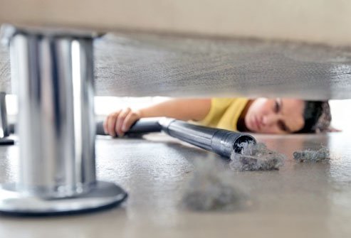 a woman vacuuming dust underneath her bed