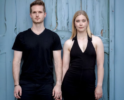 Ein Bild, das den Kontrast zwischen der modernen schwarzen Kleidung des Paares und dem verwitterten, blauen Holz der Tür hervorhebt, fotografiert in Bad Langensalza mit der EOS R5M2 & dem RF 85mm f1.2