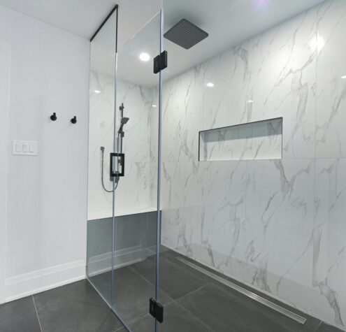 Modern bathroom with glass-enclosed shower and marble walls, showcasing a 2025 Ontario basement renovation design trend.