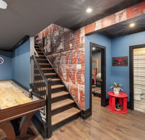 Modern basement game room blending 2025 trends: rustic brick, stairway, and a sleek game table in an Ontario renovation.