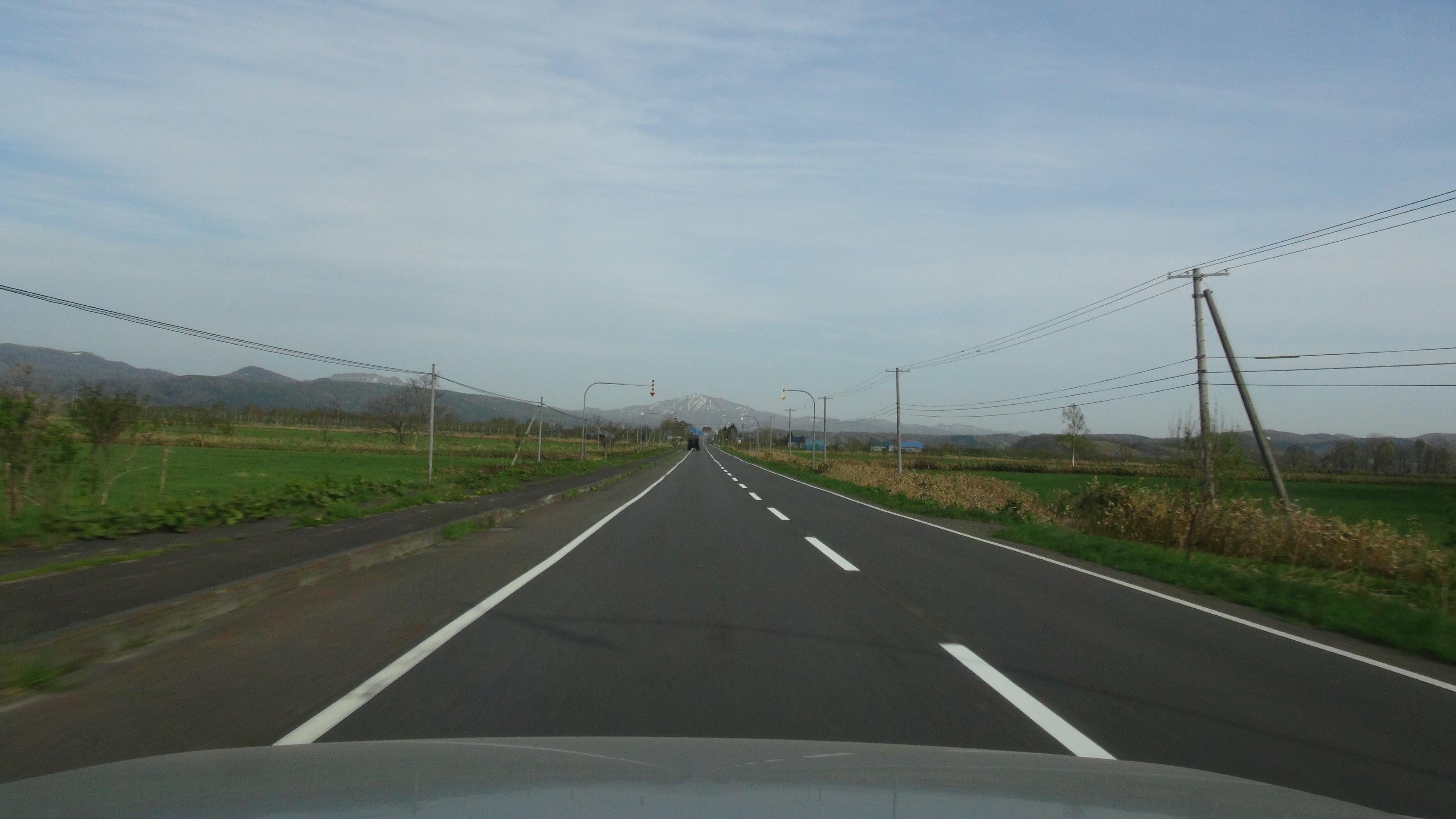 北海道の農地と残雪の山が見える直線道路