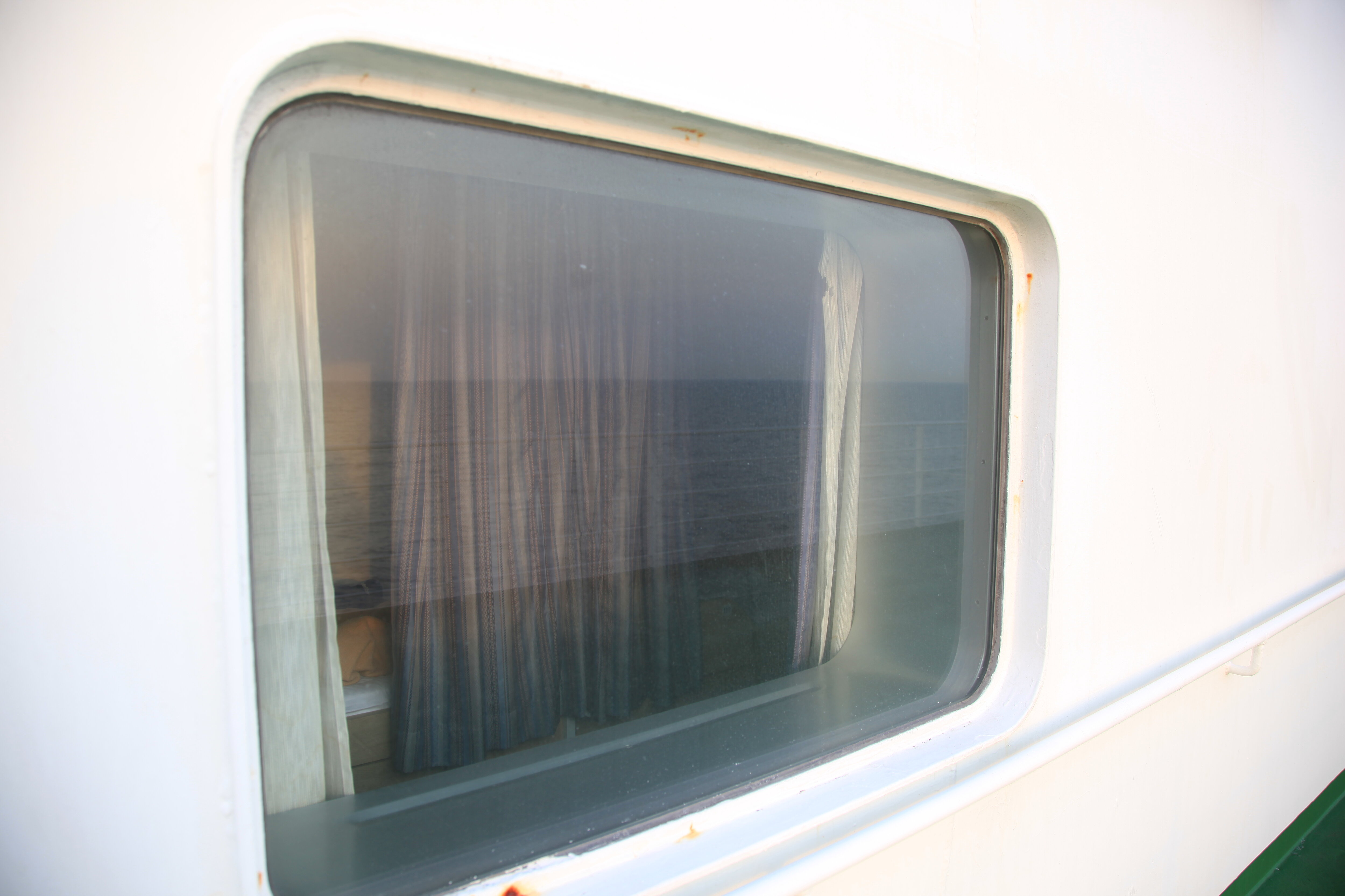 船室窓のカーテンと朝の海