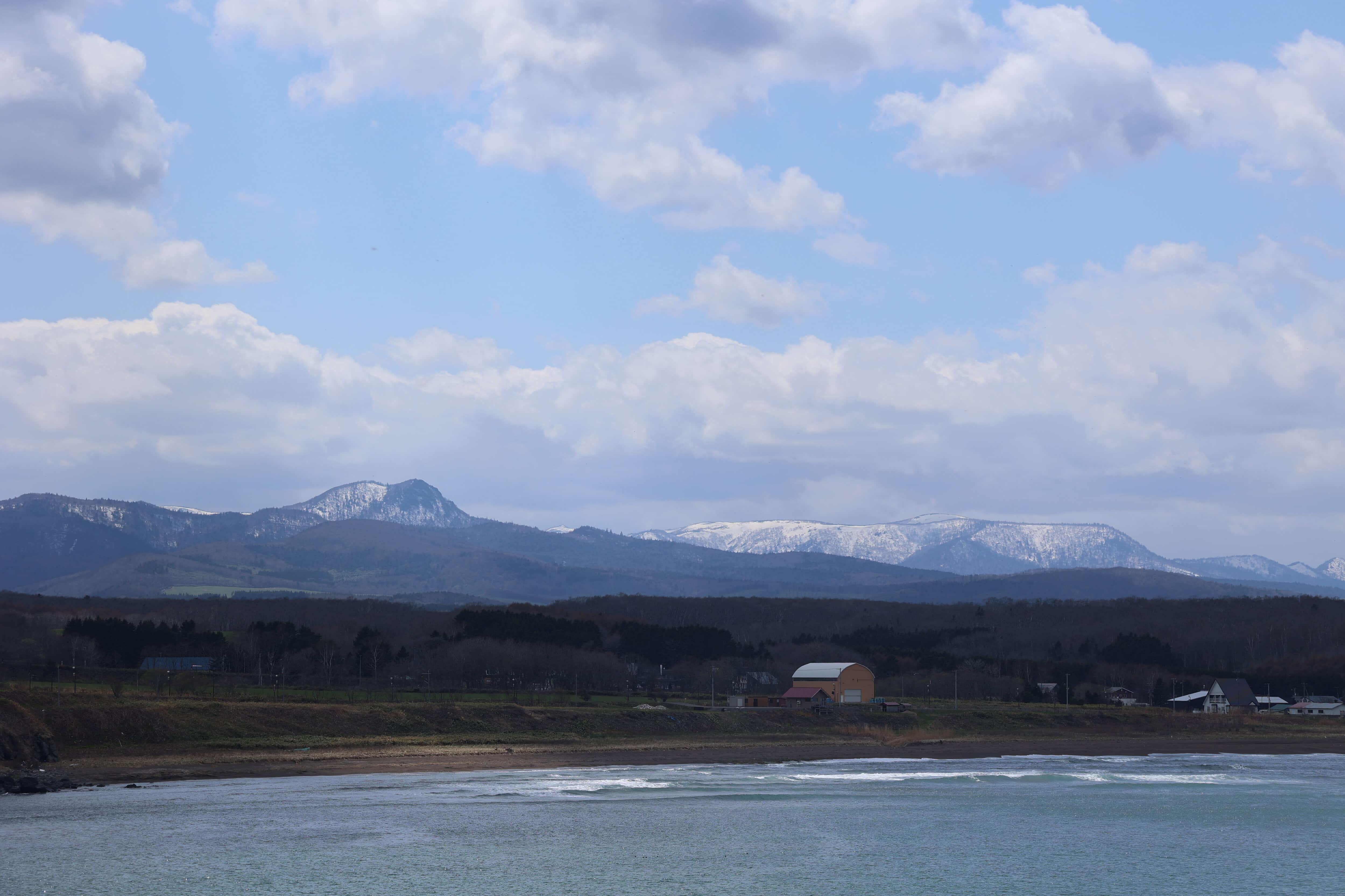 25.日の出岬・残雪の山と海岸集落の遠望（望遠）