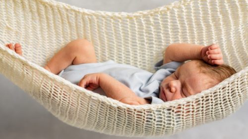 Newborn baby sleeping in a cream-colored, crocheted hammock.