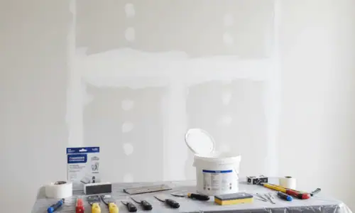 Handyman repairing drywall with tools and patch on wall