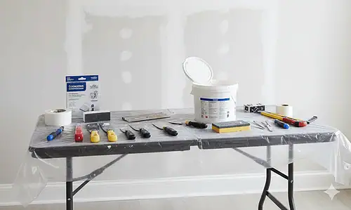 Handyman repairing drywall with tools and patch on wall