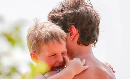 Upset crying child clinging tightly to an adult for comfort
