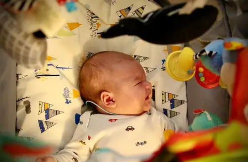 Infant crying uncomfortably surrounded by hanging baby toys