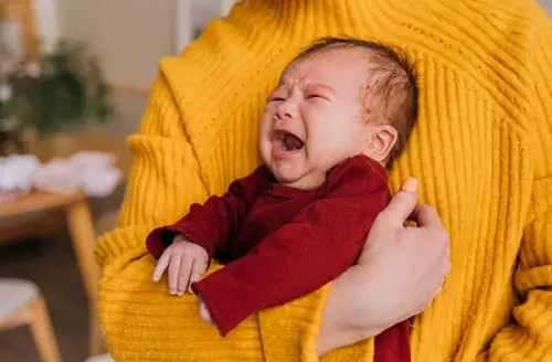 Newborn wailing loudly while being held in adult arms