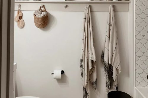 Bathroom shelf and hook rail styled with a woven basket, striped fringed towels, and a small art print — bathroom towel rack basket decor ideas from the By Paige Nicole blog.