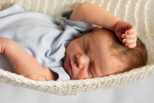 Newborn baby sleeping in a cream-colored, crocheted hammock.