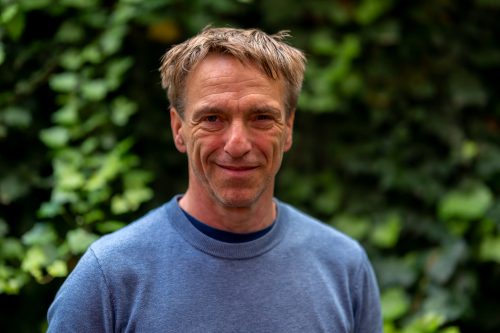 Ein freundlicher Stadtführer für eine Stadtführung Freiburg vor einer grünen Efeuwand. Der Mann trägt einen blauen Pullover und lächelt in die Kamera.