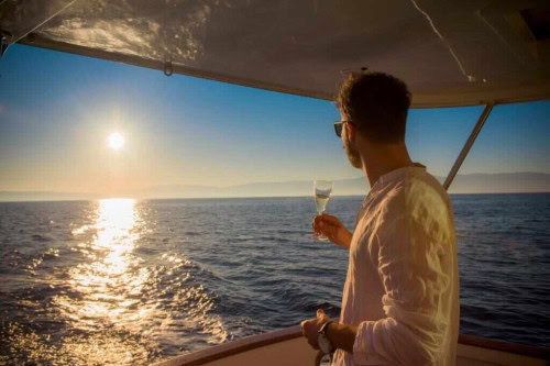 Man enjoying a luxury private boat tour from Opatija at sunset with a glass of champagne