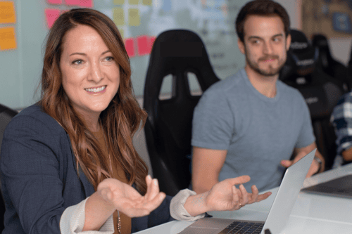 A man and a woman working and talking together with an open laptop in front of the woman.