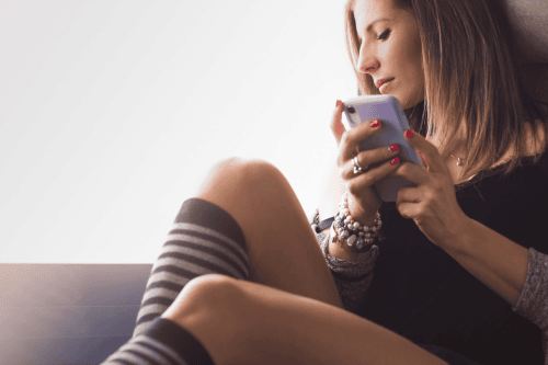 Featured photo of woman holding phone and looking out the window, thinking.