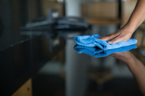 hand wiping a glossy surface with a blue microfiber cloth, illustrating the difference between wiping for appearance and proper surface cleaning in commercial spaces done by a professional commercial cleaning company like AMC Commercial Cleaning