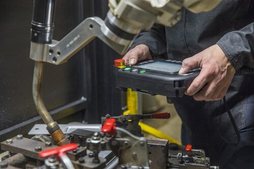 Closeup of weld cell supervisor programming robot with teach pendant