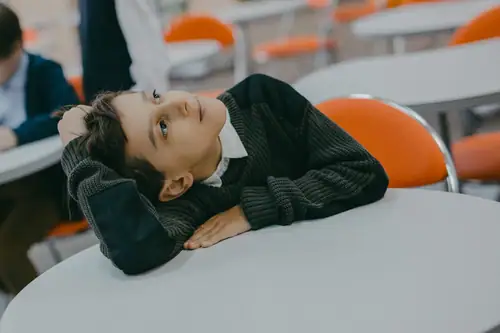 Boy lies listlessly on classroom table, distracted and evasive