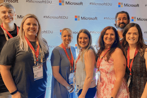 7 professionals smiling in front of microsoft banner