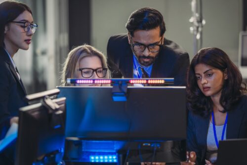 Professionals collaborate in tech environment. Senior members coaching, mentoring, guiding colleagues through data analytics and software development. Knowledge sharing, leadership, technical growth