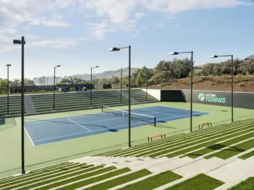Outdoor tennis court featuring stadium-style seating, professional lighting, and landscaped surroundings under a clear blue sky in Raleigh.