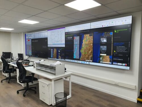Imagen del video wall de 10 pantallas en la sala de monitoreo de CGE Talca, con mapas en tiempo real y sistemas de alerta desplegados en pantalla.