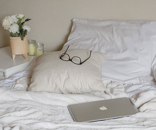 Glasses on a pillow with a laptop on a white bed