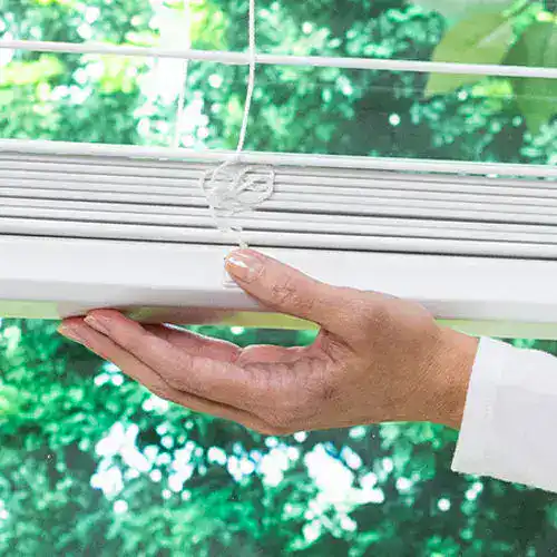 Close-up of a hand cleaning window blinds with a cloth outdoors.