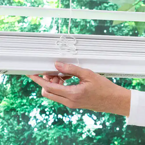 Close-up of hand holding window blind in bright indoor setting.