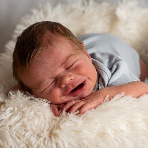 Close-up of a newborn baby sleeping and smiling on a soft, white furry blanket.