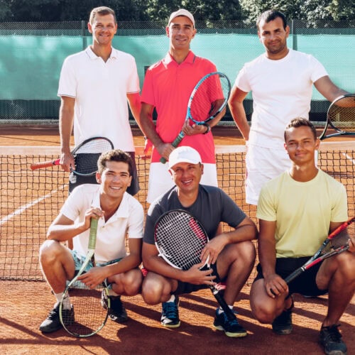 Group portrait of six male tennis players standing on court