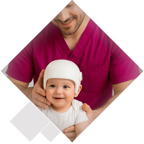 Fisioterapeuta con pijama sanitario color fucsia sosteniendo suavemente a un bebé sonriente con casco ortopédico para tratar la plagiocefalia