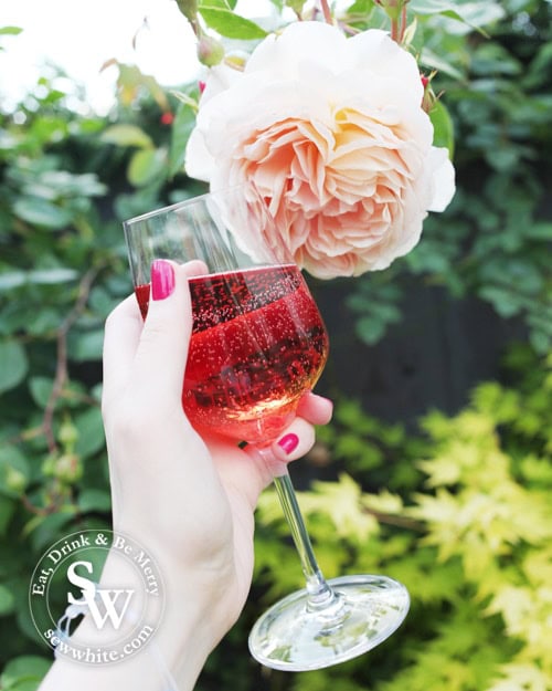 Holding a glass of rose in the garden next to a flower in the Top Rose wines for summer