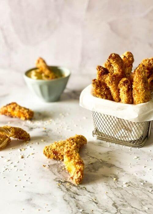 chicken fries in a container with parchment paper on a marble background, more fries around and panko, behind a bowl with mayo