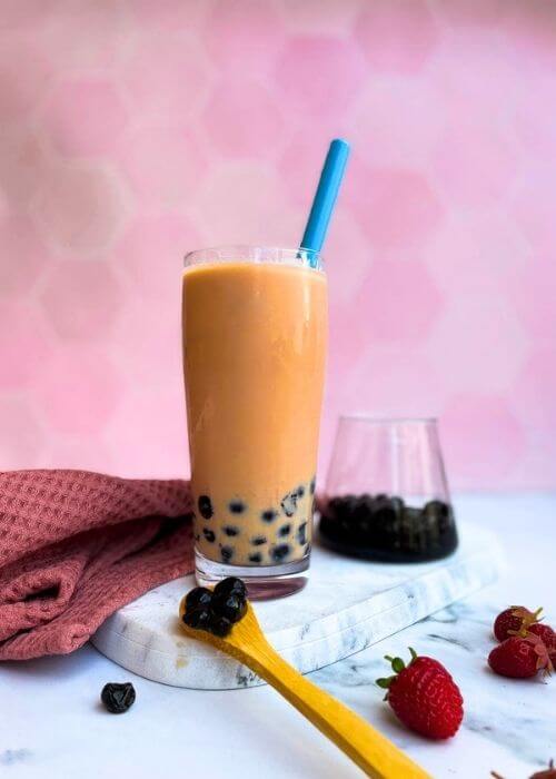a strawberry milk tea on a marble tray with a glass of boba on pink background