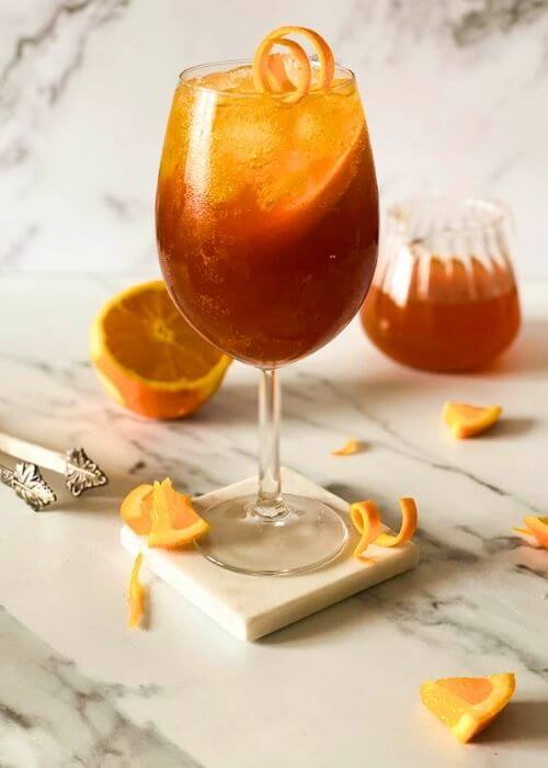 Super Aperol Spritz Mocktail, Just Like The Real One 5 close up, aperol spritz mocktail, marble background, ice tongues and slices of orange around and a jug of liquid