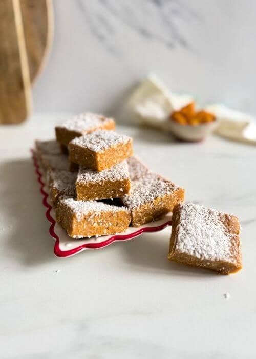 on a plate more apricot slice, behind a bowl of apricots, towel and two wooden boards on a marble background