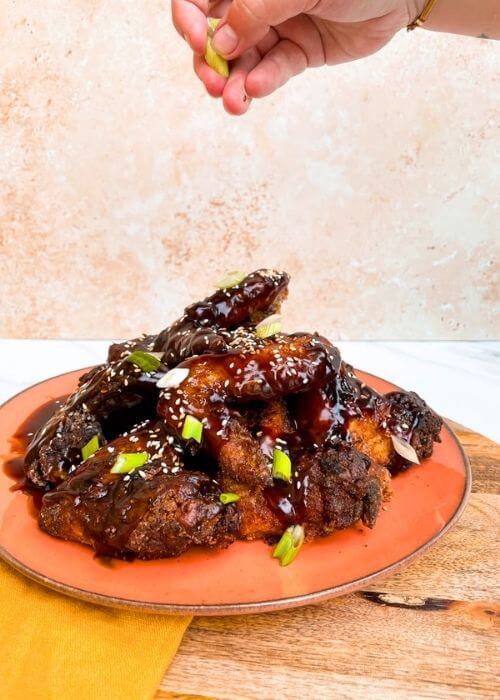 hand holding onions = soy garlic chicken wings on a plate, on a wooden board and yellow towel